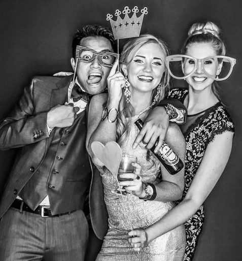 Three people dressed up, wearing fun glasses and props in a photo booth