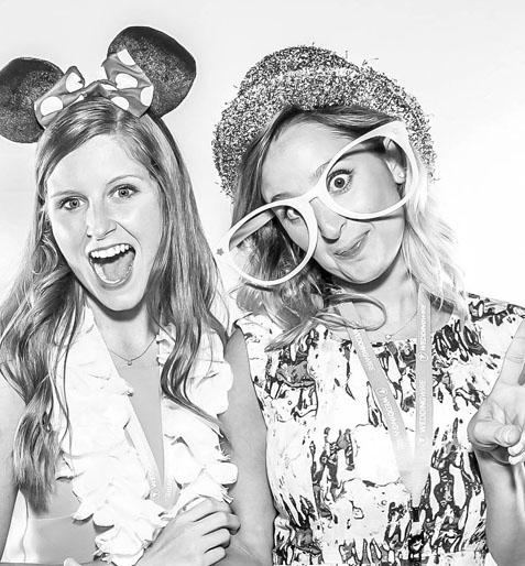 Two women wearing fun props, including Mickey Mouse ears and oversized glasses, in a photo booth