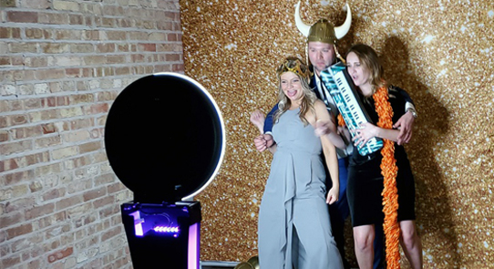 Group of people posing with props in front of a photo booth with a gold glittery backdrop