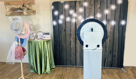 Photo booth setup with a rustic wooden backdrop and a table of props including hats and signs