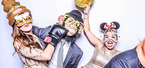 Group of people having fun with photo booth props, including a poop emoji hat, boxing gloves, monkey mask, and Mickey Mouse ears